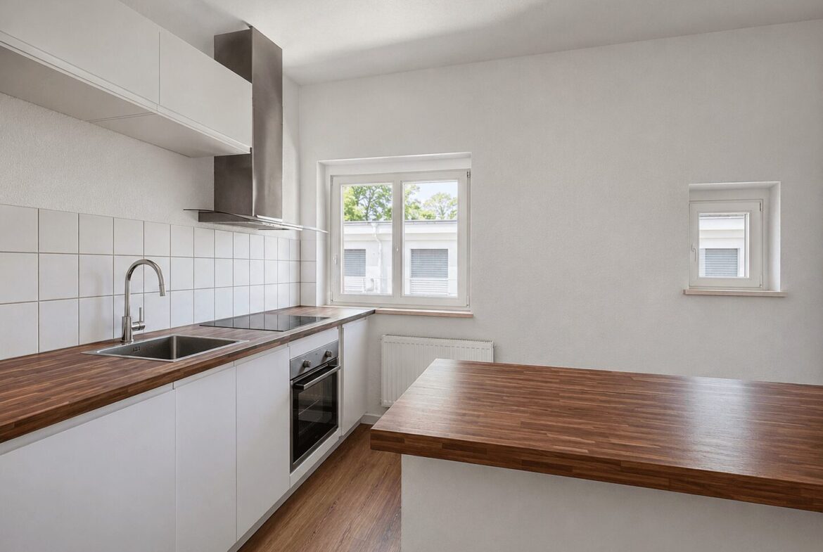 White kitchen with wood countertops, stainless steel sink, built-in oven, and a breakfast island under ample natural light from two windows