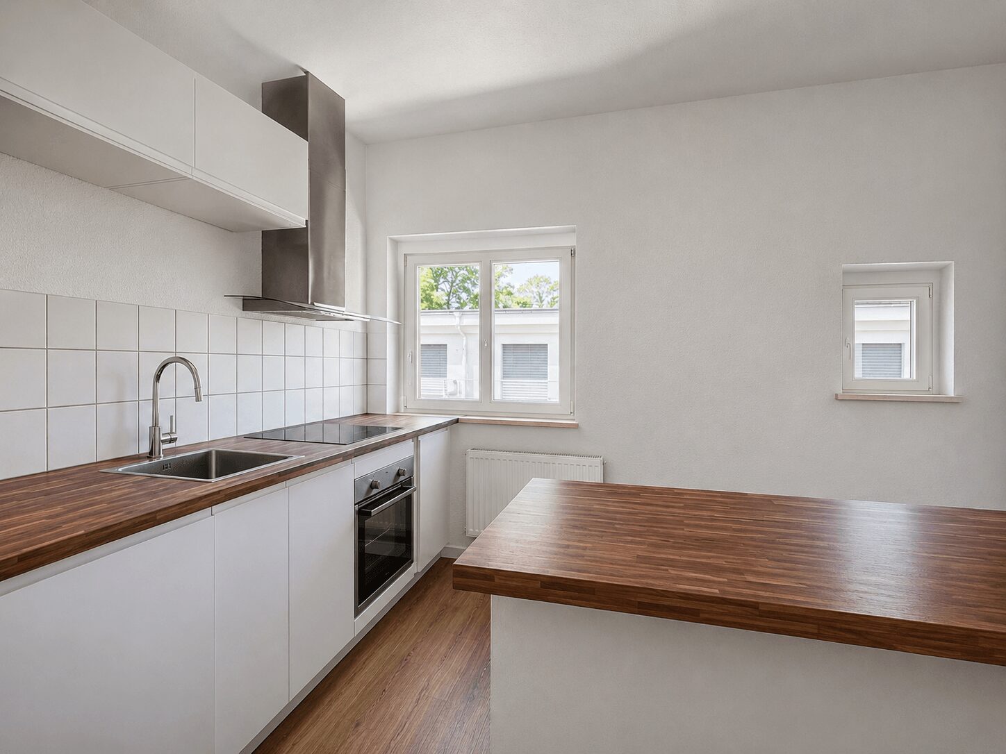White kitchen with wood countertops, stainless steel sink, built-in oven, and a breakfast island under ample natural light from two windows