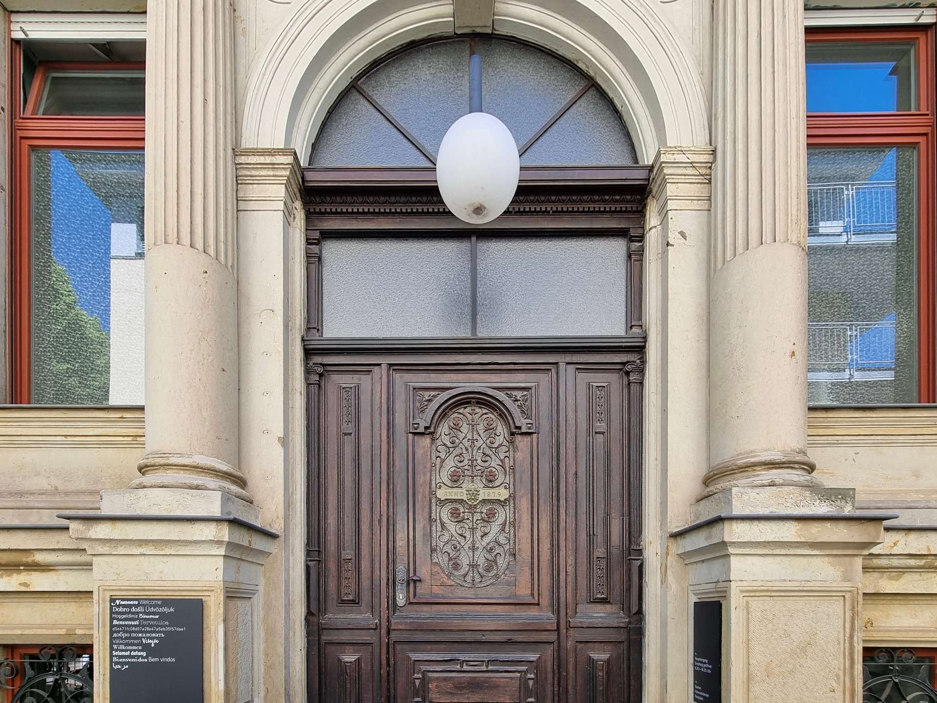 Front entrance of a historic building with a large carved wooden door, fluted columns, and a white oval light fixture above.