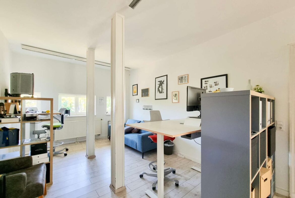 Open-plan office with desks, chairs, and wall art; a partition and shelving unit separate work areas.