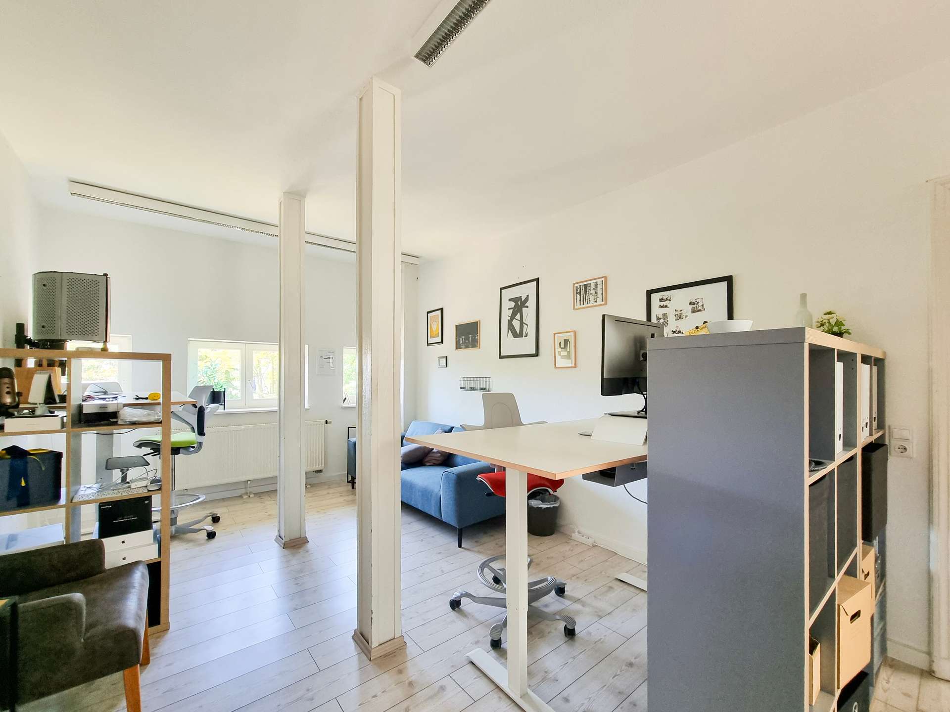 Open-plan office with desks, chairs, and wall art; a partition and shelving unit separate work areas.