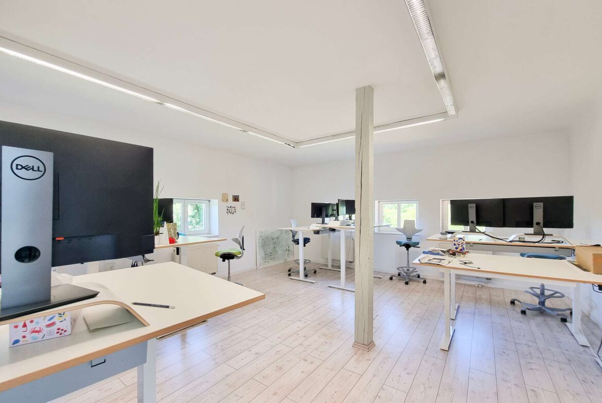 Open-plan office with white desks, ergonomic chairs, and a Dell computer tower in the foreground.