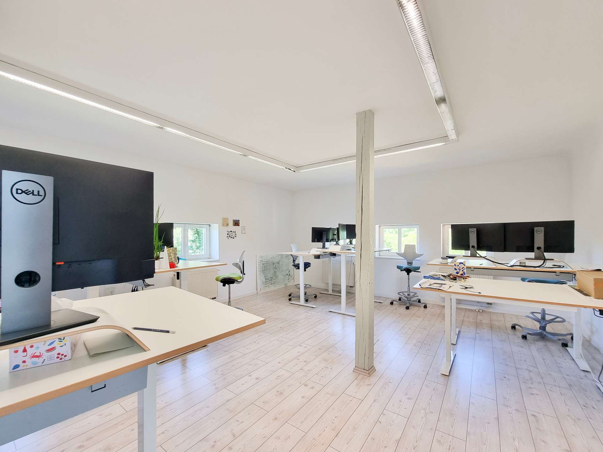 Open-plan office with white desks, ergonomic chairs, and a Dell computer tower in the foreground.