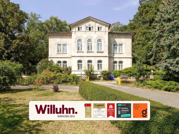 Beige two-story villa with arched windows, flanked by tall trees and a well-kept garden.