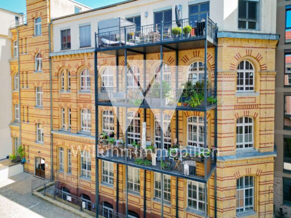 Brick apartment building with ornate arches and multiple balconies on each floor, metal railing and potted plants outside windows