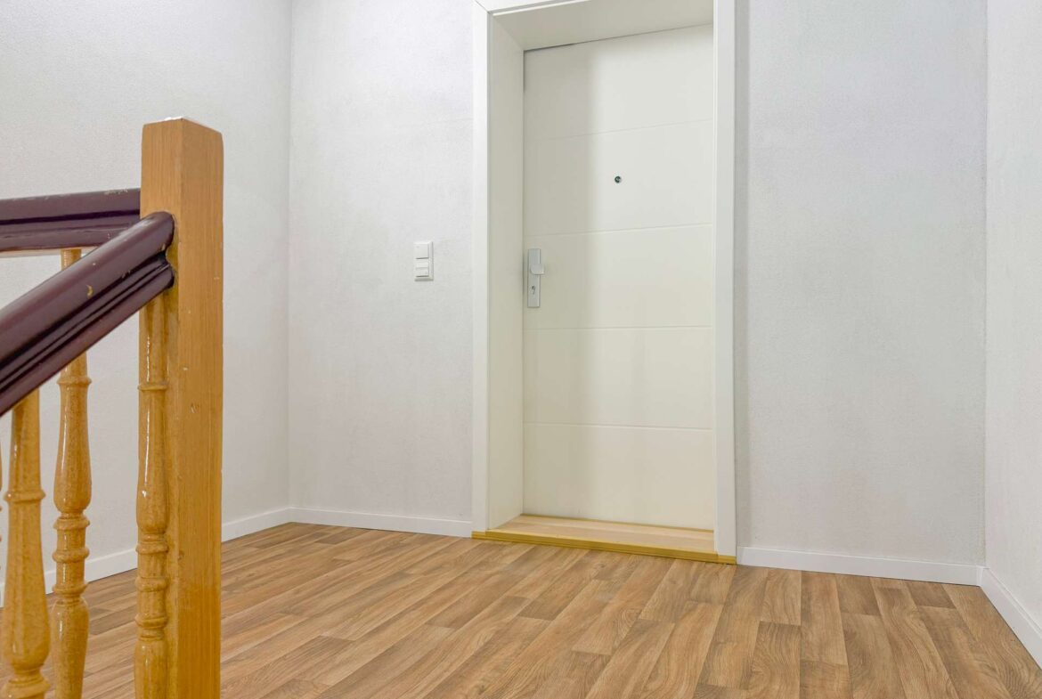 Interior stair landing with a wooden balustrade on the left and a white interior door at the top of the stairs.