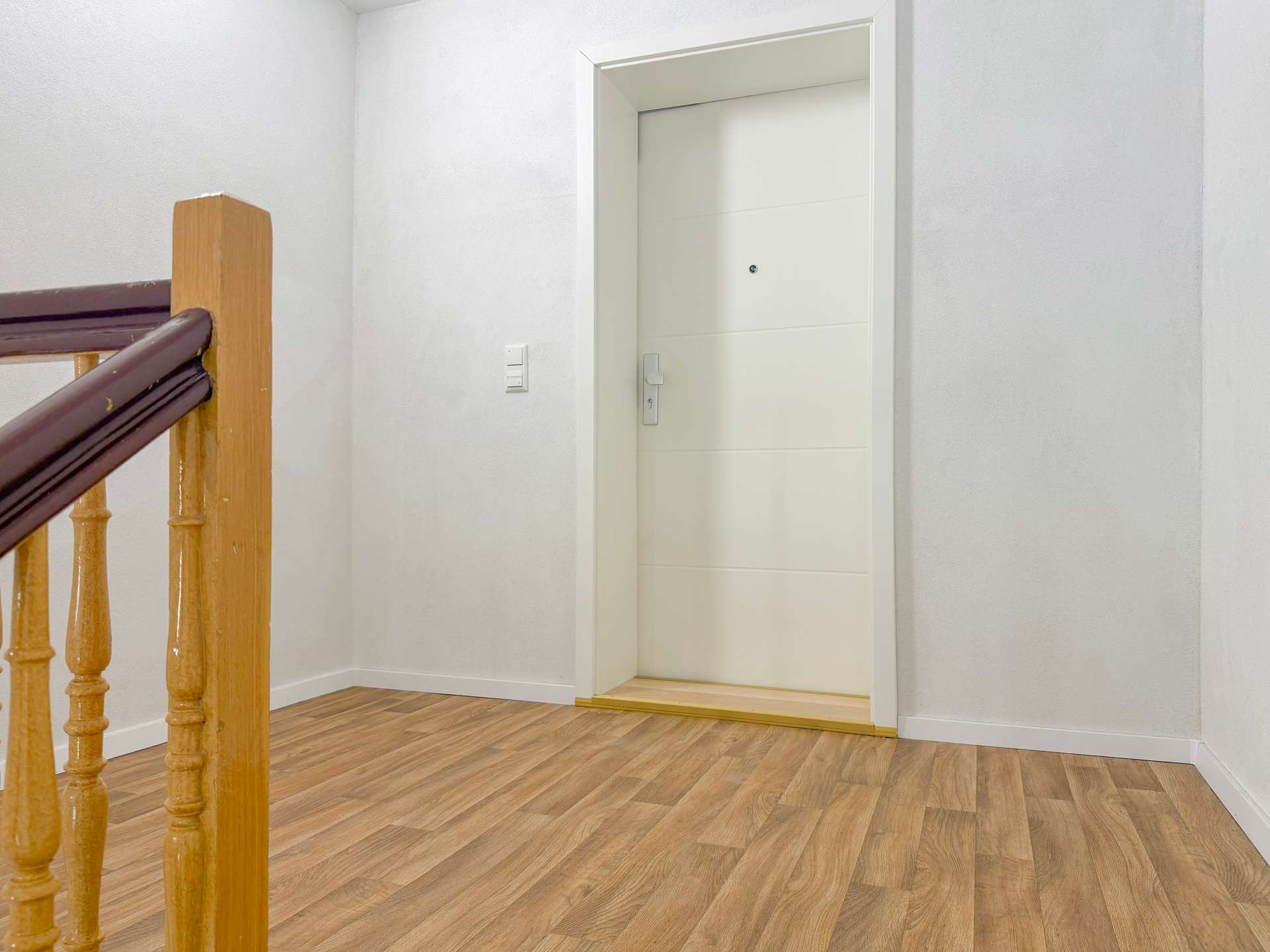 Interior stair landing with a wooden balustrade on the left and a white interior door at the top of the stairs.