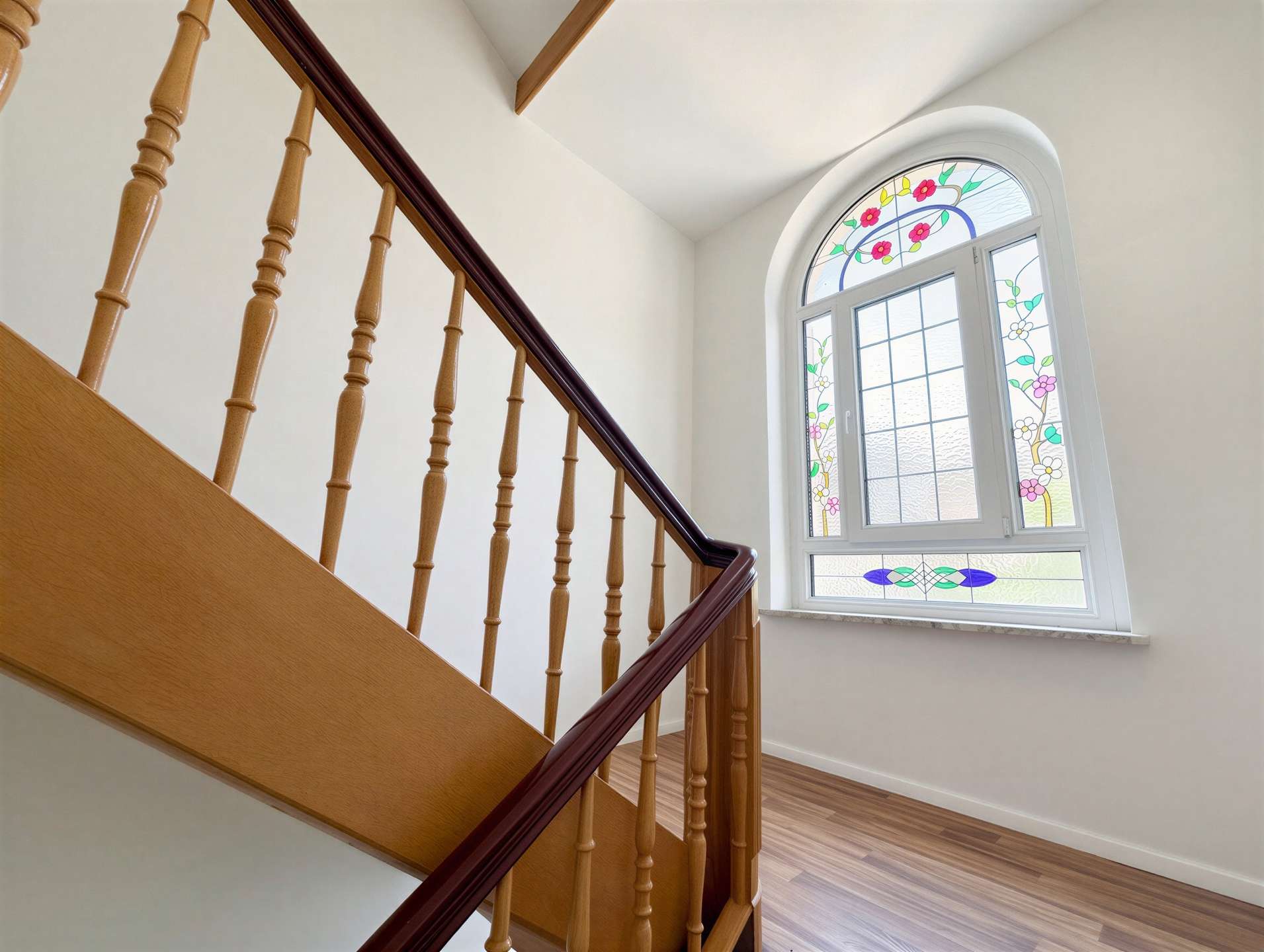 Wooden staircase with turned balusters and a dark handrail beside a large arched stained-glass window.