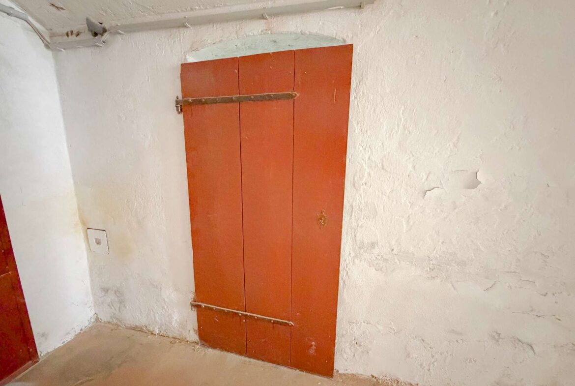 Orange-painted wooden door panel with a metal bar across it, in a rough plaster-walled utility basement room.