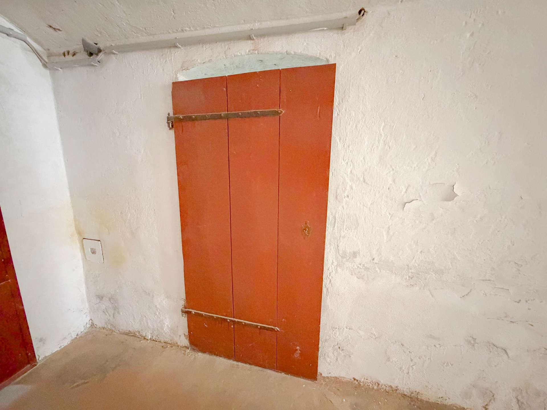 Orange-painted wooden door panel with a metal bar across it, in a rough plaster-walled utility basement room.