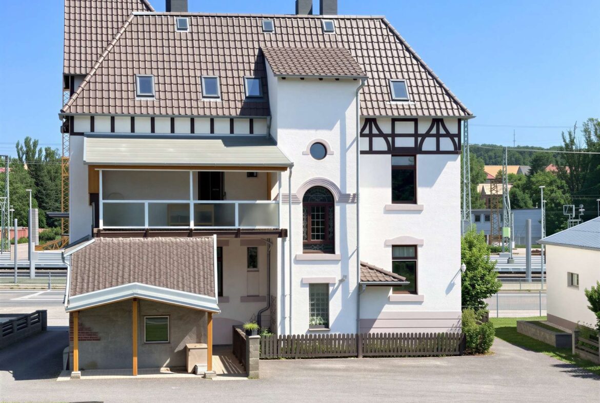 White, multi-story house with a steep brown tile roof, dormer windows, and a circular window above the entrance.