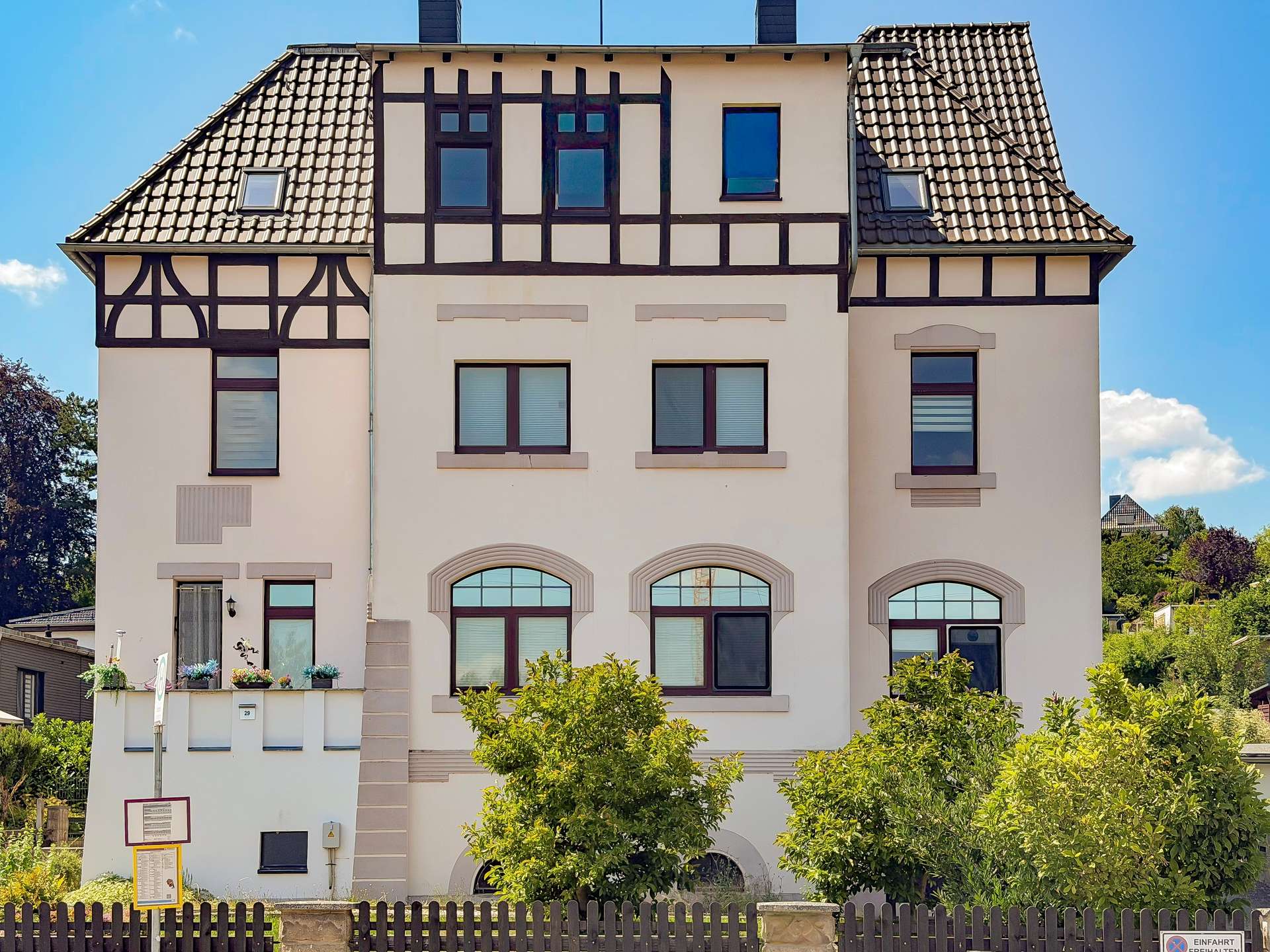 Front view of a beige, Tudor-style building with dark timber framing, large arched ground-floor windows, and a blue sky above.