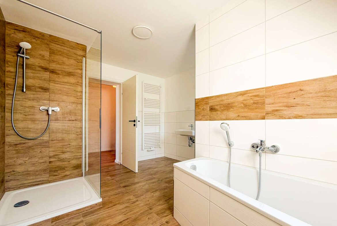Modern bathroom with a glass shower enclosure, wood-look wall tiles, and a white bathtub with chrome fixtures.