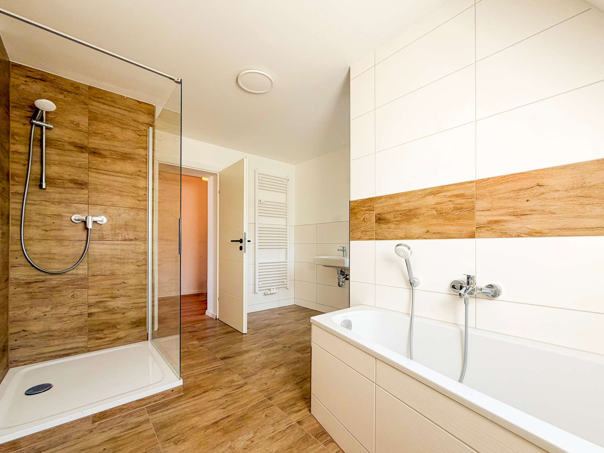 Modern bathroom with a glass shower enclosure, wood-look wall tiles, and a white bathtub with chrome fixtures.