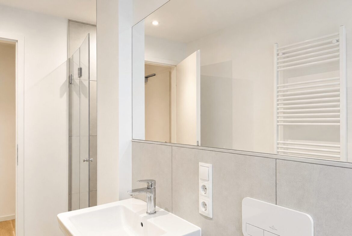 Modern bathroom with square white sink, chrome faucet, large wall mirror, and a white towel warmer on the wall.