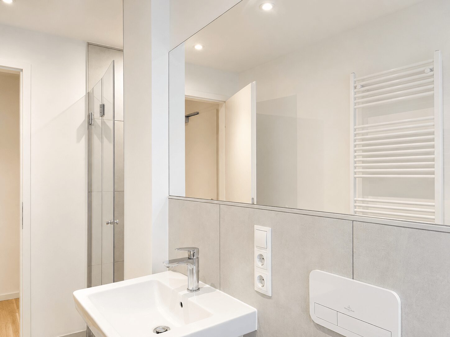 Modern bathroom with square white sink, chrome faucet, large wall mirror, and a white towel warmer on the wall.