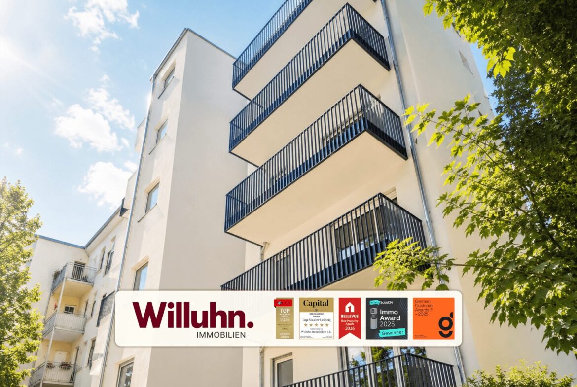 White apartment building with stacked blue rail balconies, sunny sky, and trees; a Willuhn Immobilien banner at the base.