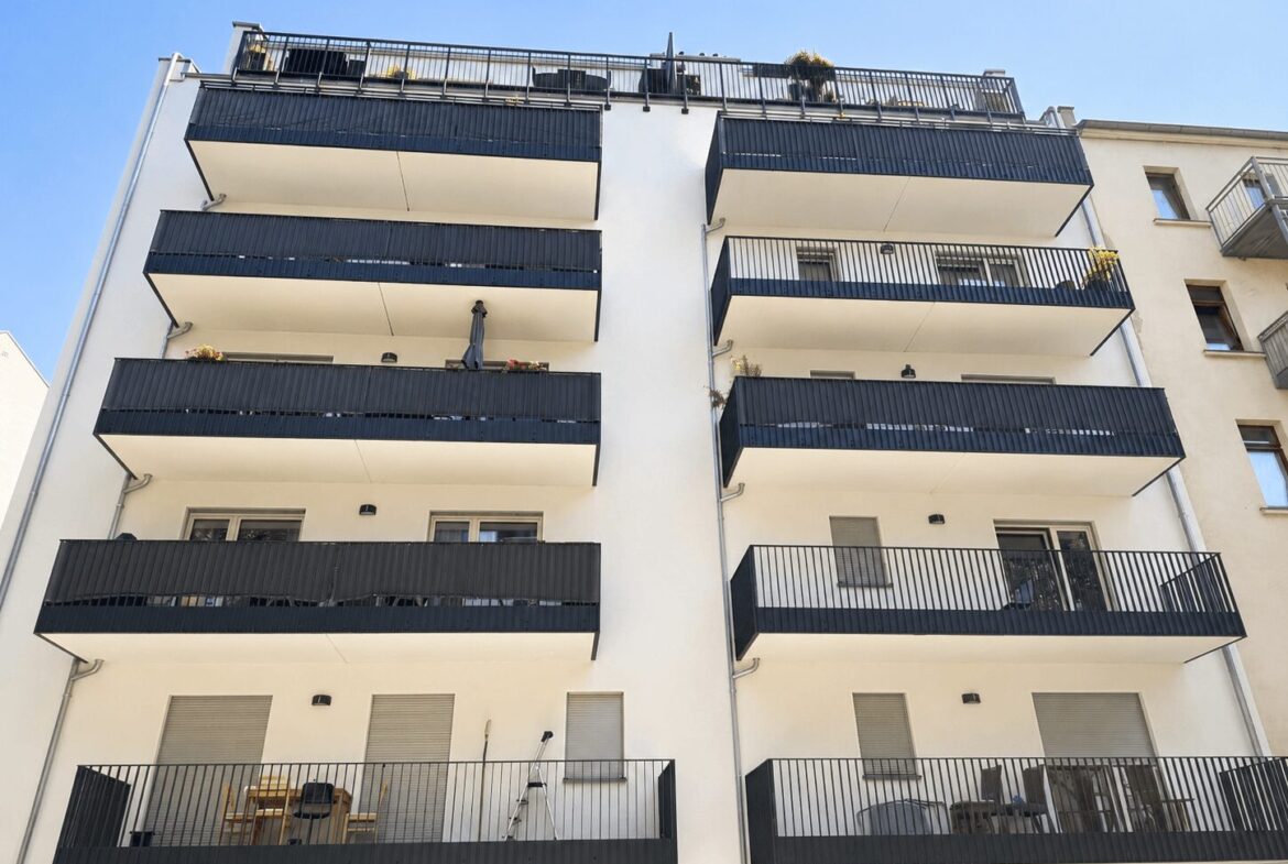 White apartment building with multiple blue-railed balconies stacked on two towers against a clear blue sky.