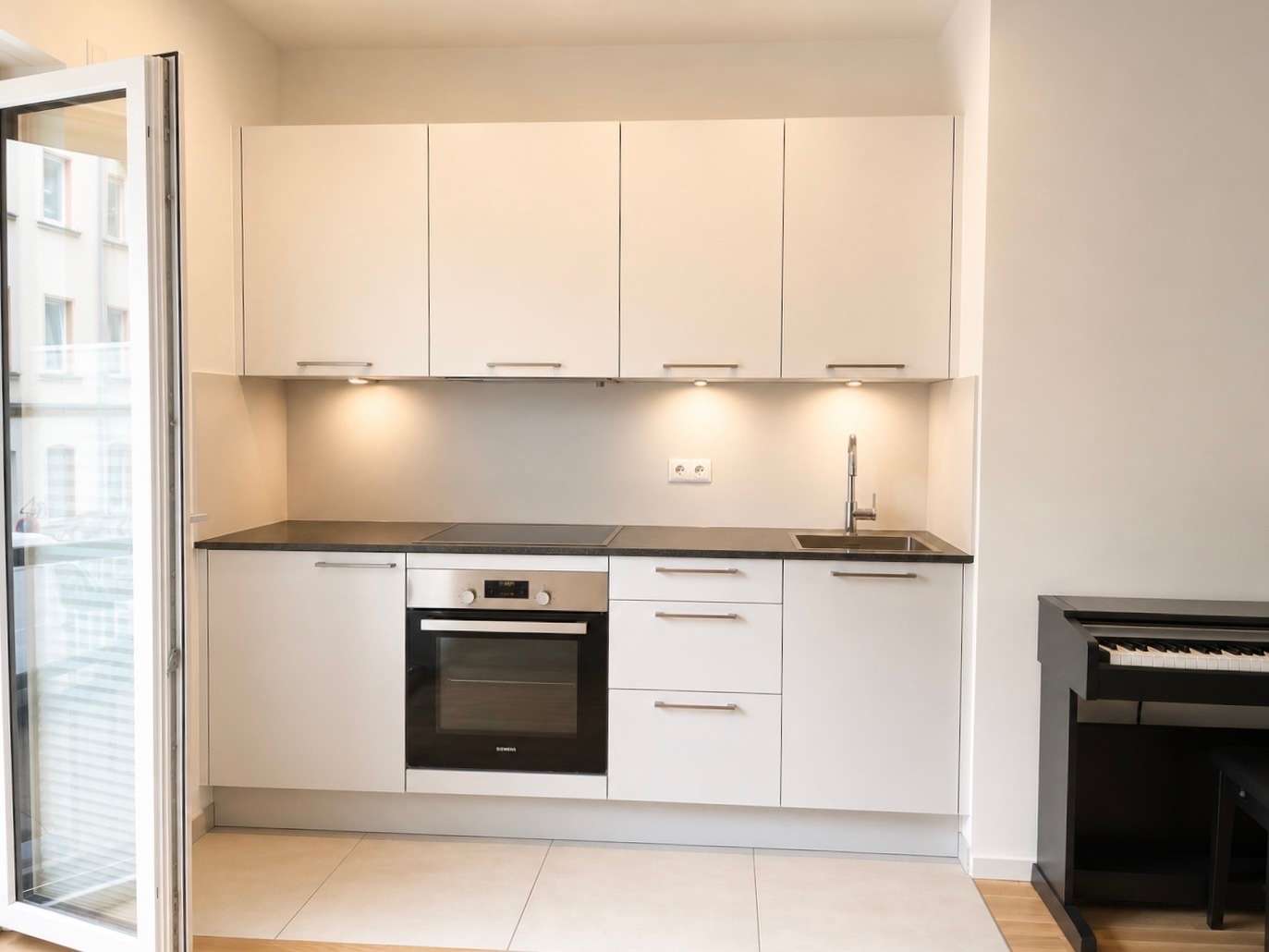 Modern white kitchen with upper and lower cabinets, built-in oven, stovetop, sink, and under-cabinet lighting.