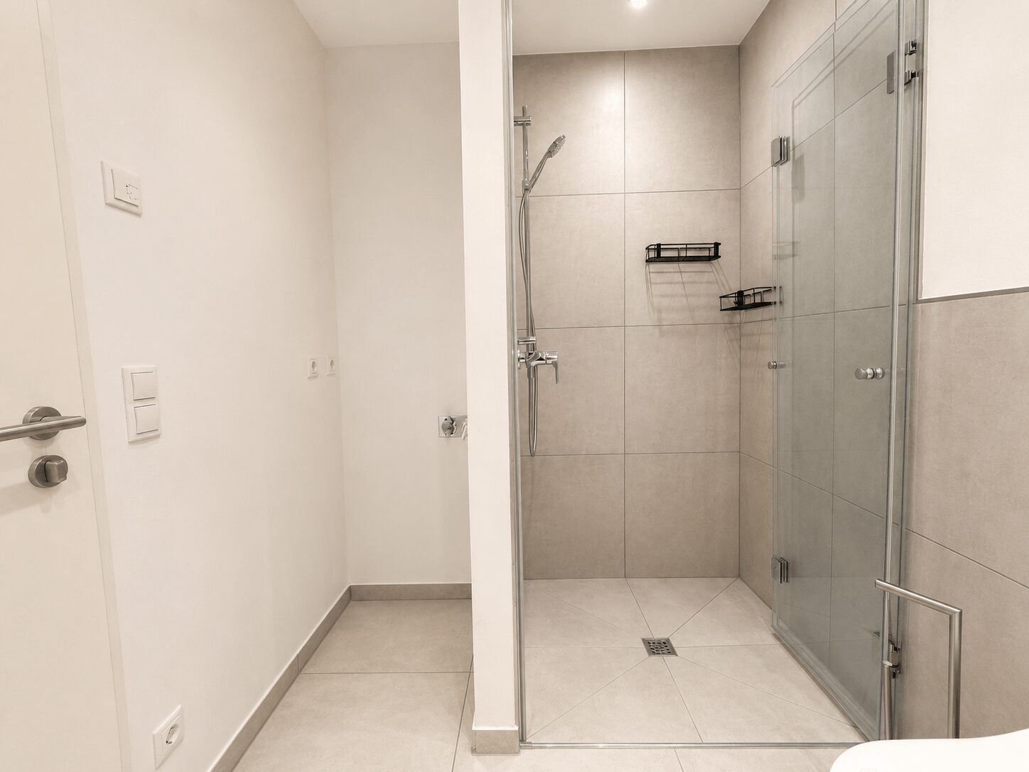 Modern bathroom entrance showing a glass shower enclosure with tiled walls and chrome fixtures.