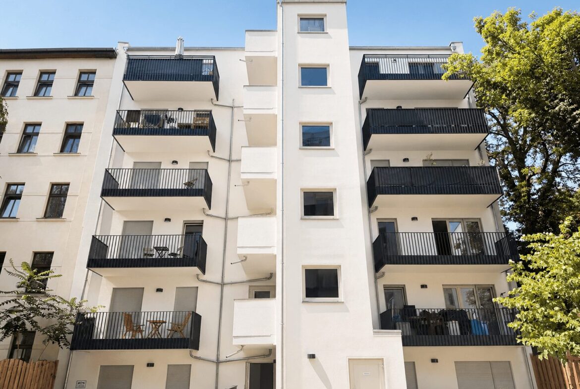 White modern apartment building with six stories, black railings, and blue sky appears above.