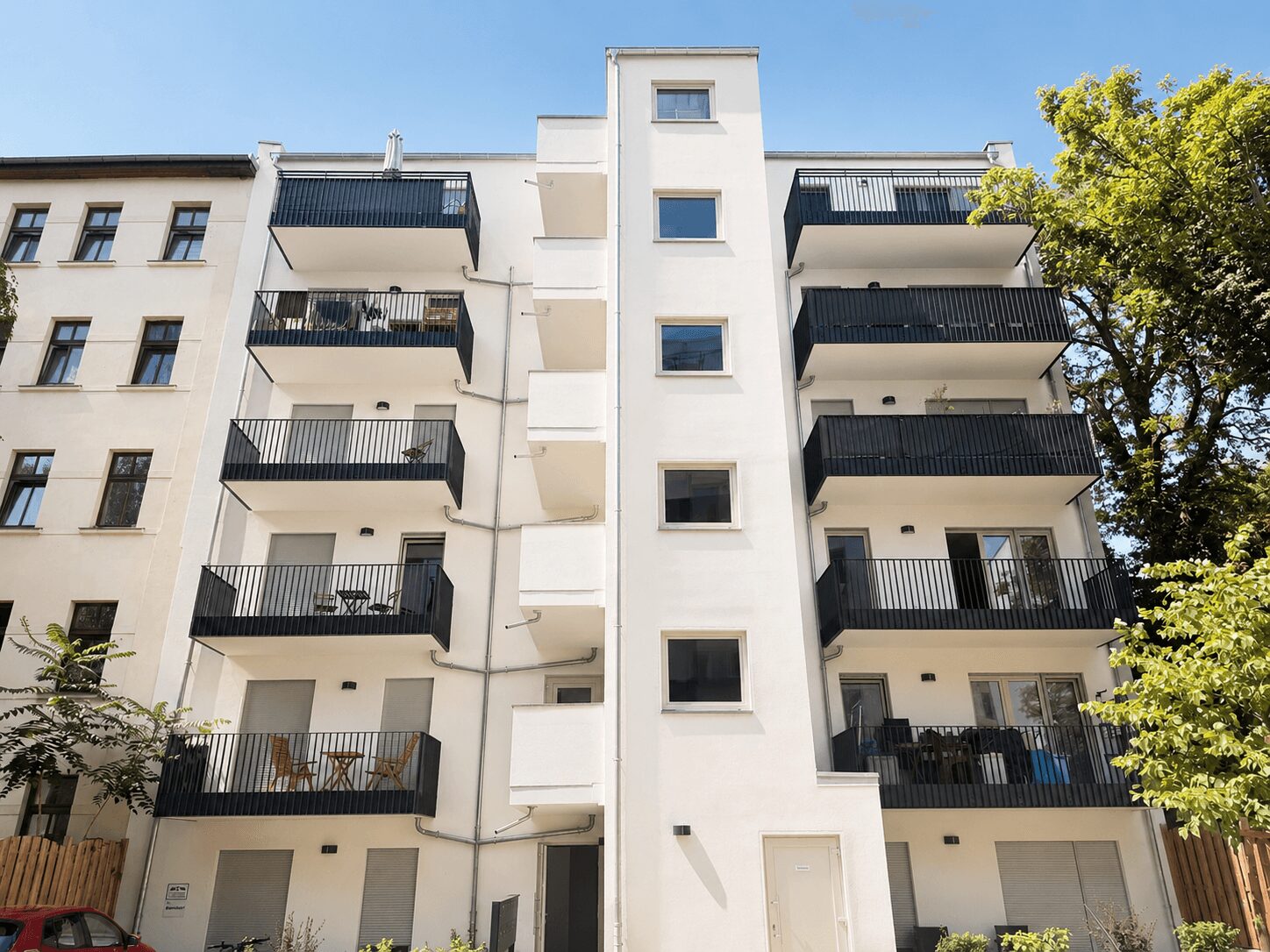 White modern apartment building with six stories, black railings, and blue sky appears above.