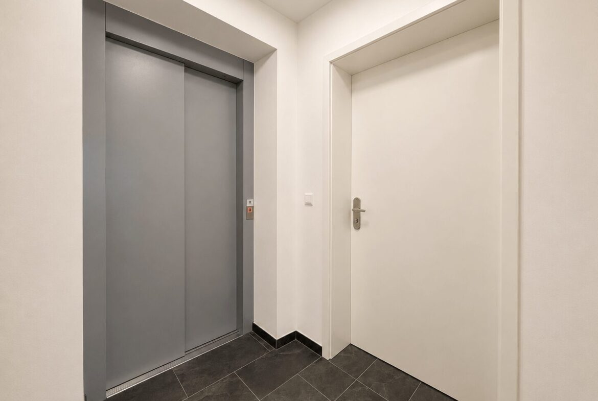 Interior hallway with closed gray elevator doors on the left and a white door on the right, dark tiled floor.