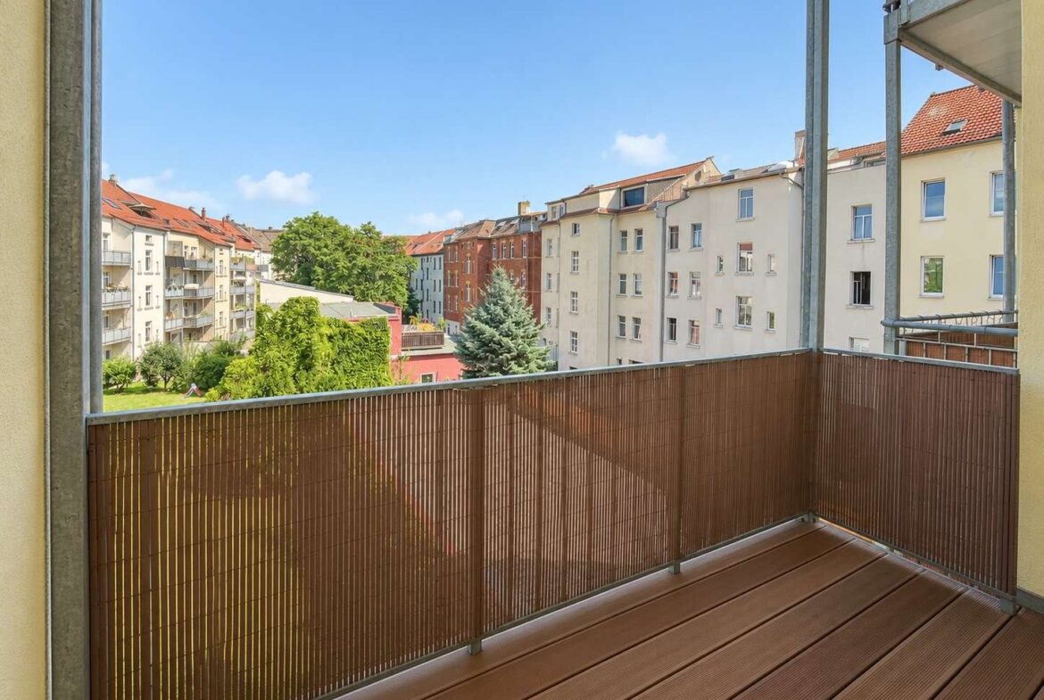 View from a balcony looking onto a row of midrise apartment buildings with a green courtyard and blue sky above.
