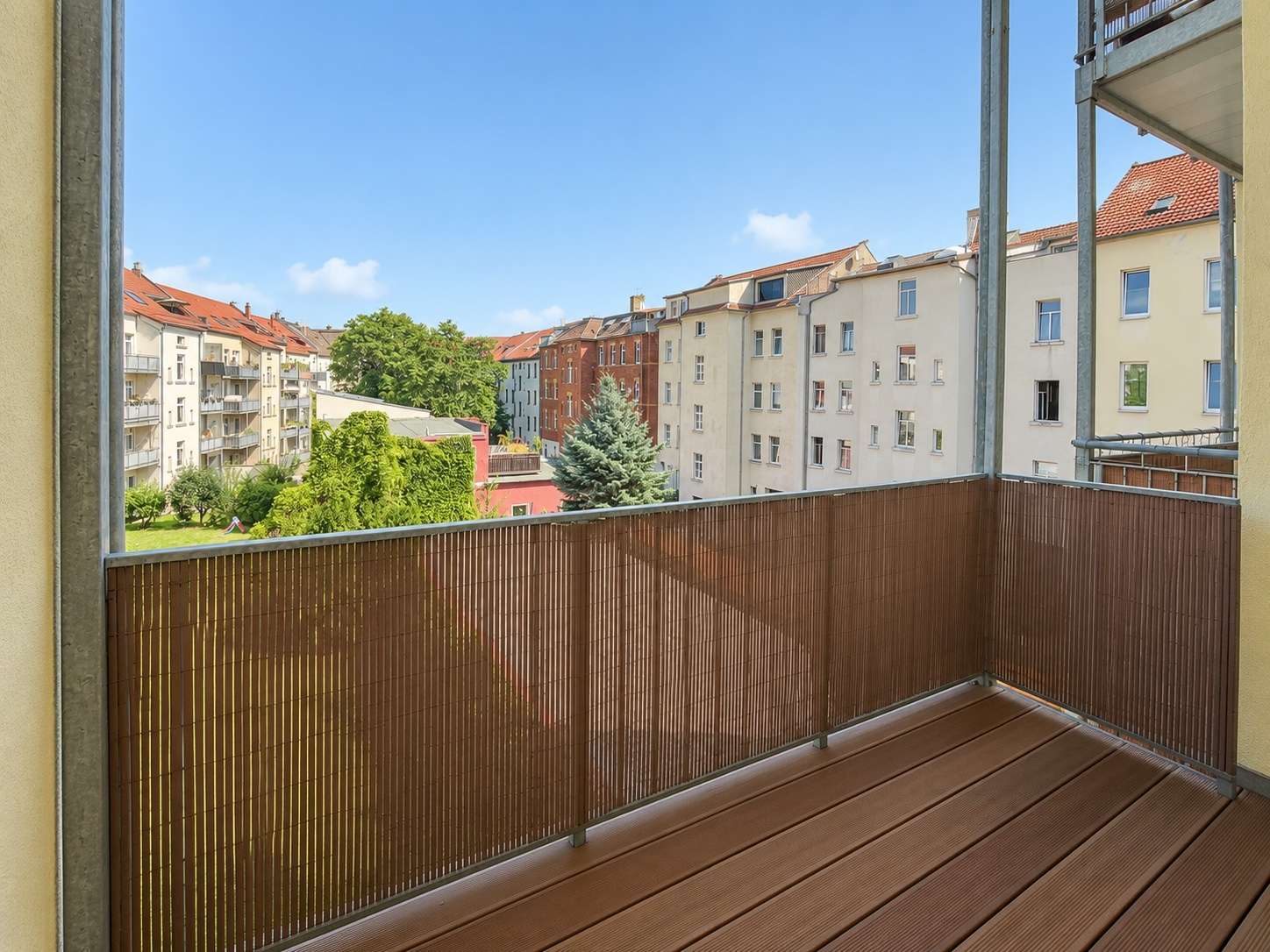 View from a balcony looking onto a row of midrise apartment buildings with a green courtyard and blue sky above.
