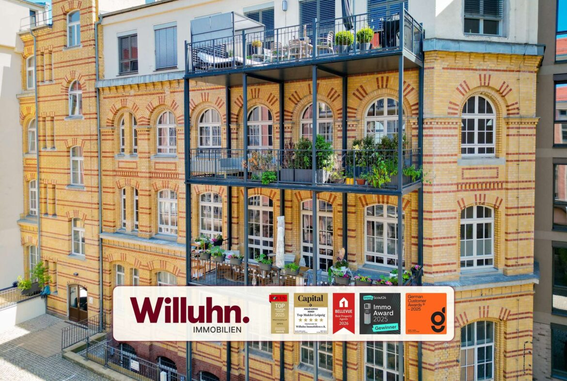 Brick apartment building featuring arched windows and a metal balcony structure; a large Willuhn Immobilien banner is displayed on the lower level advertising the property company.