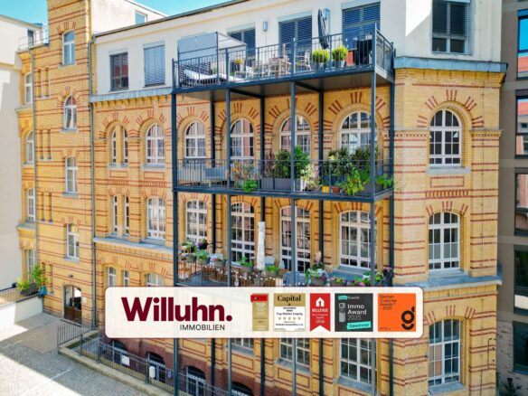 Brick apartment building featuring arched windows and a metal balcony structure; a large Willuhn Immobilien banner is displayed on the lower level advertising the property company.