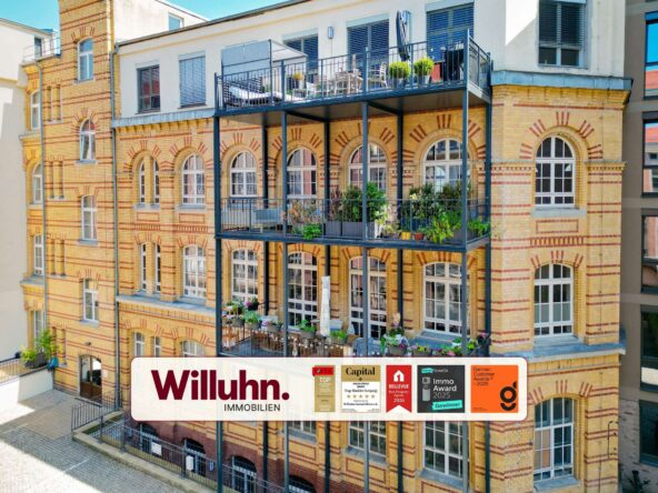 Brick apartment building featuring arched windows and a metal balcony structure; a large Willuhn Immobilien banner is displayed on the lower level advertising the property company.