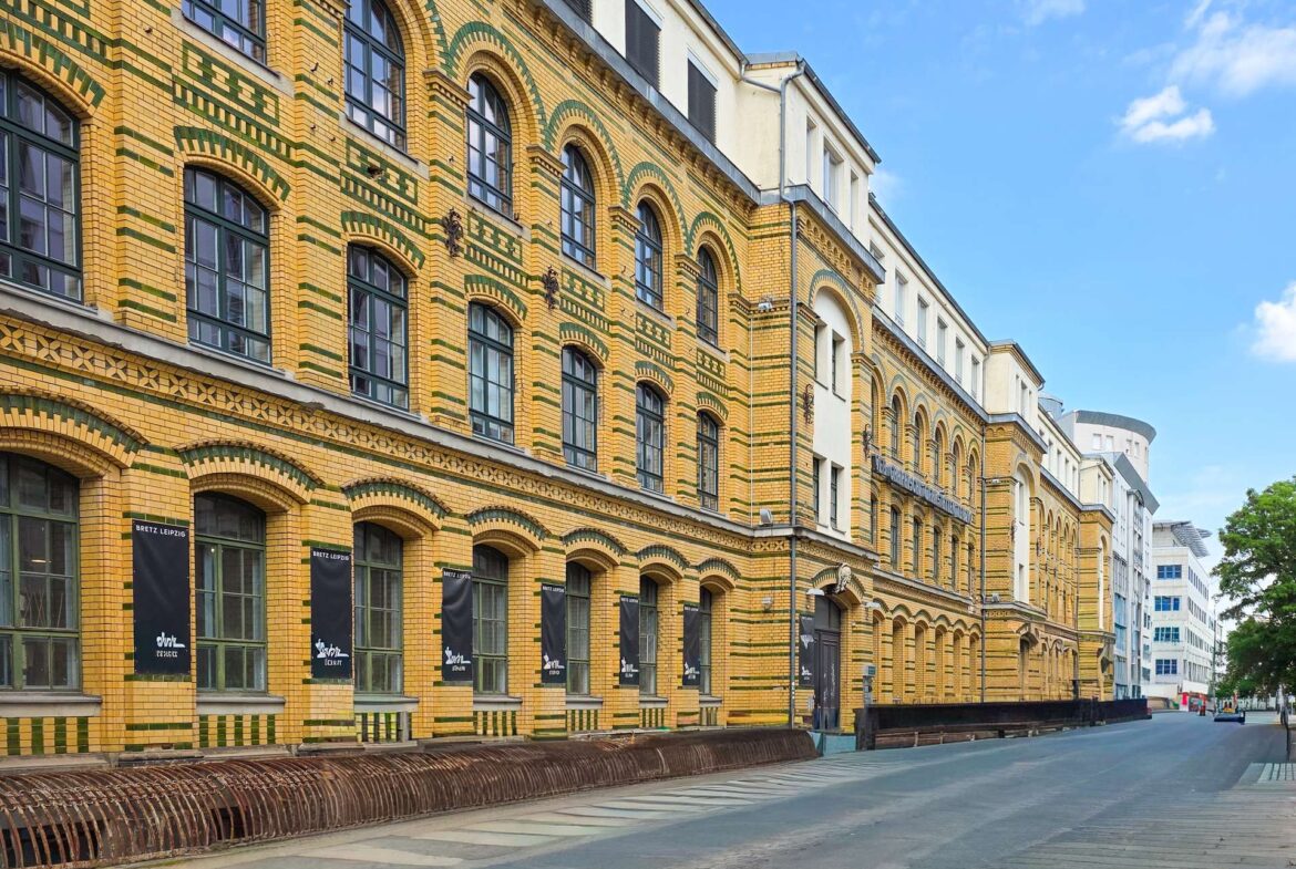 Yellow brick building with green decorative arches and large arched windows along a quiet street. (Informative)