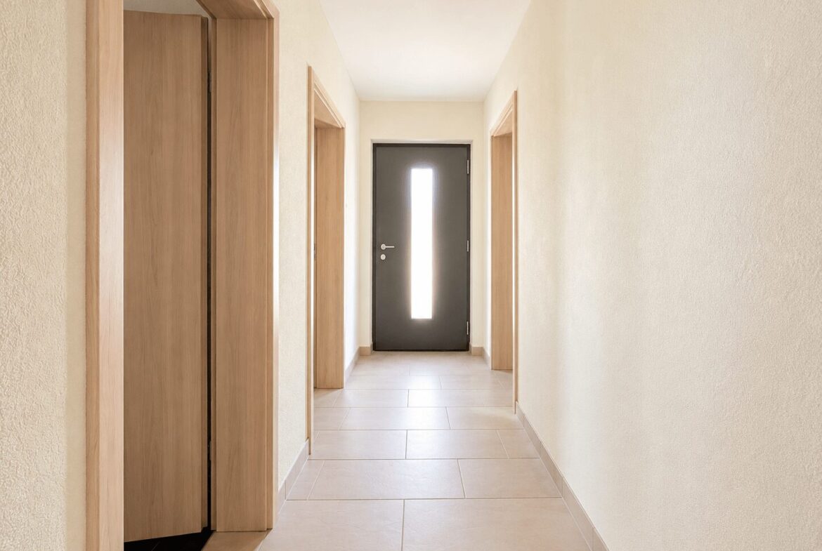 Long beige hallway with light wood doors on both sides and a dark front door with a vertical glass panel at the end.