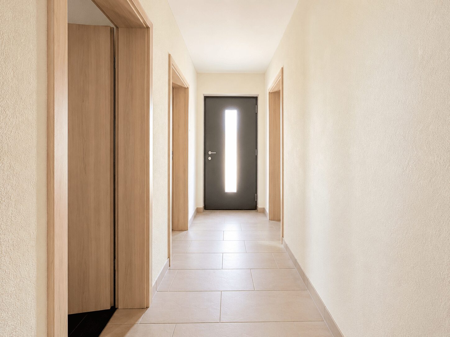Long beige hallway with light wood doors on both sides and a dark front door with a vertical glass panel at the end.