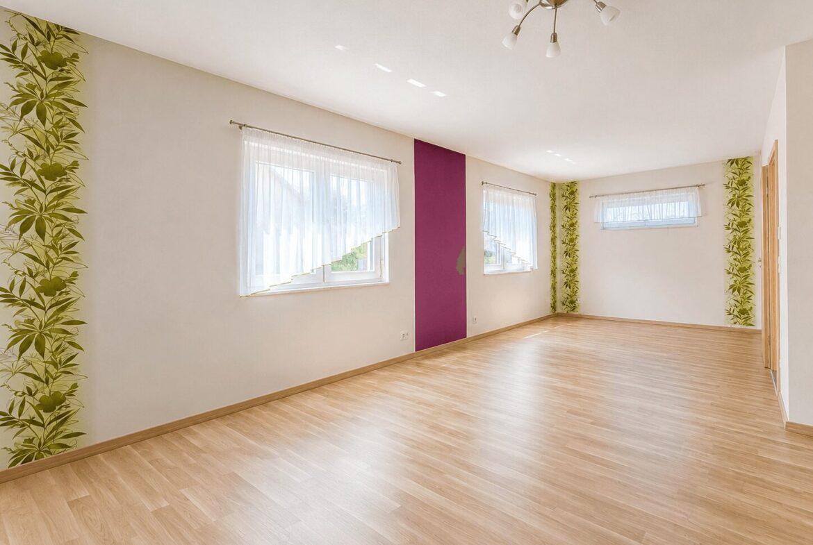 Bright empty living room with light wood flooring, white walls, purple vertical panel, and large windows with sheer curtains.