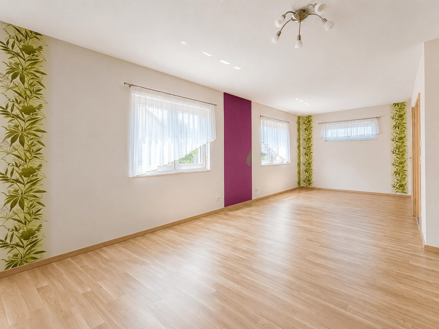Bright empty living room with light wood flooring, white walls, purple vertical panel, and large windows with sheer curtains.