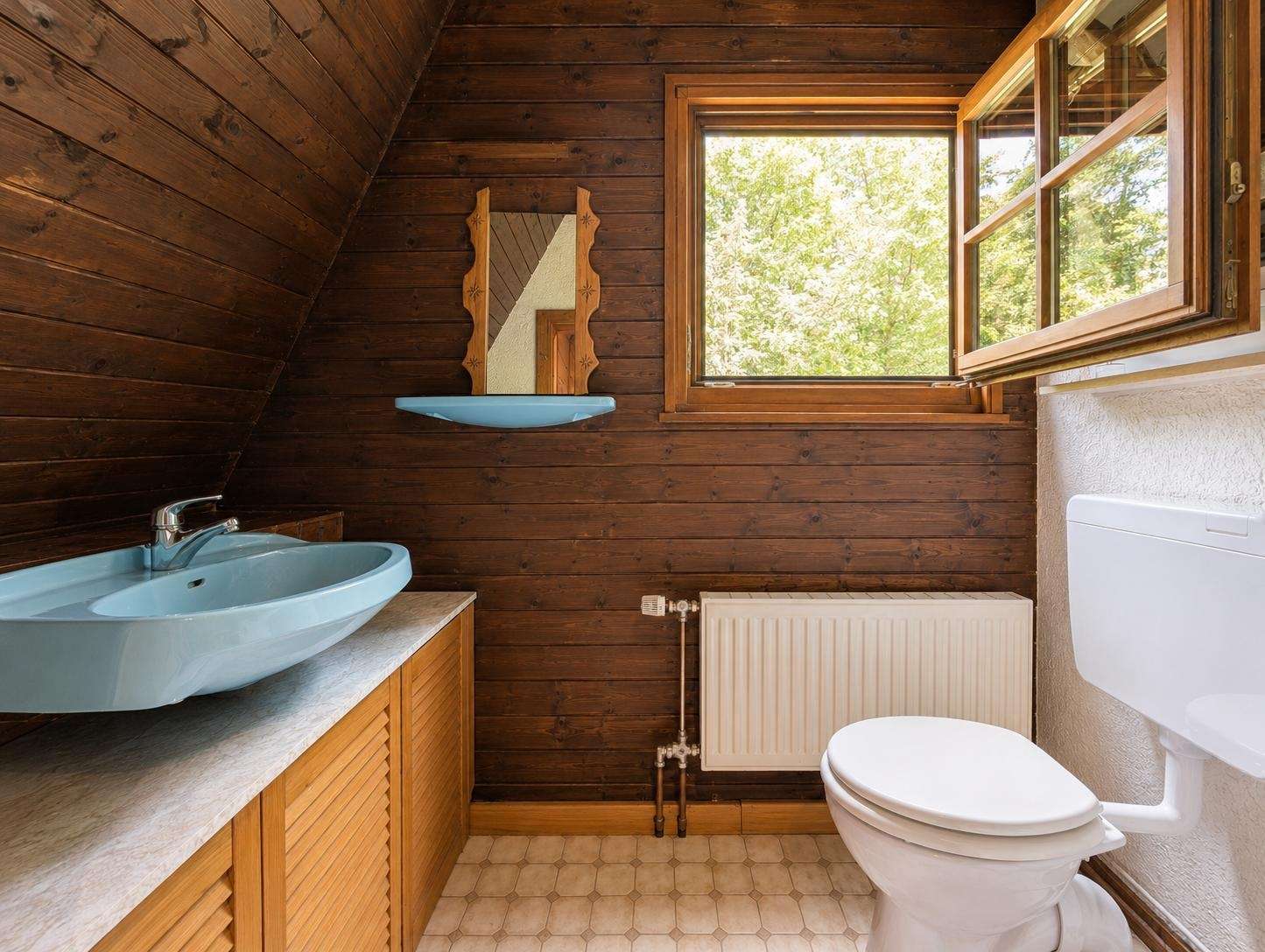 Rustic bathroom with dark wood paneling, a blue oval sink on a Marble-like countertop, and a window overlooking greenery outside.