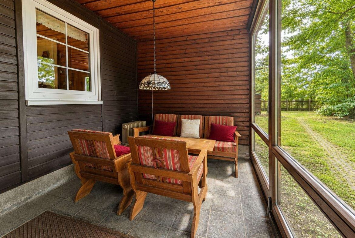 Wooden-paneled sunroom with a striped-cushion seating set around a wooden coffee table, large windows to a green yard, and a hanging Tiffany-style lamp above.