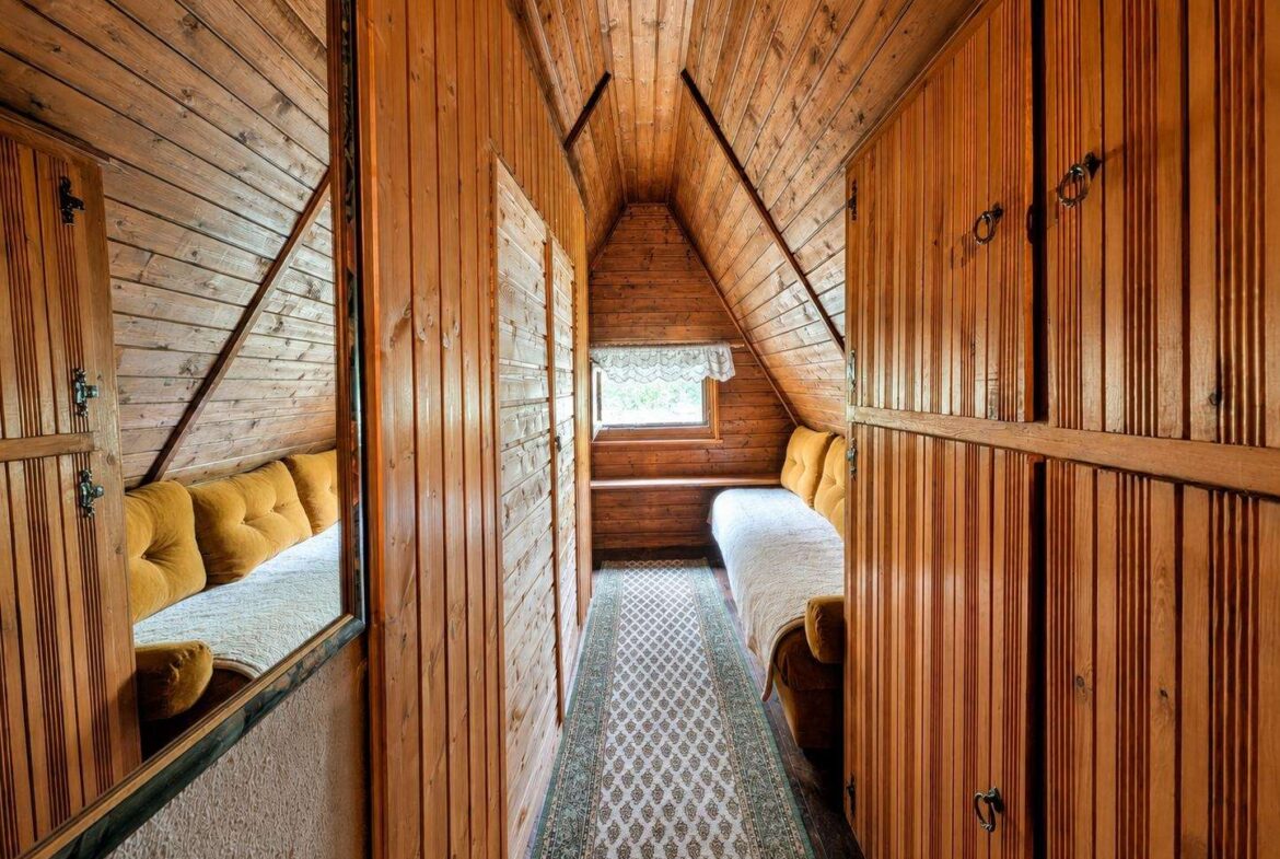 Rustic wooden attic bedroom with two single beds along opposite walls, mustard cushions, and a window at the far end.