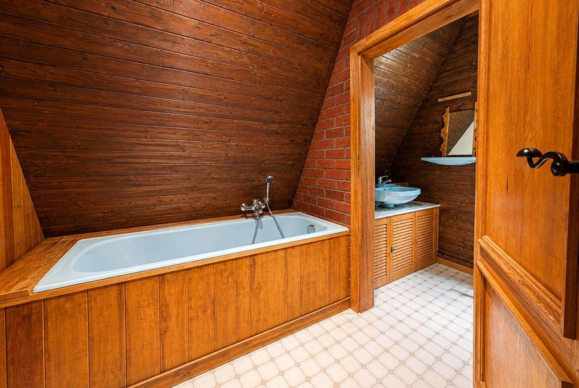 Wood-clad bathroom with a built-in white tub along a brick wall and a wooden vanity with a blue sink.