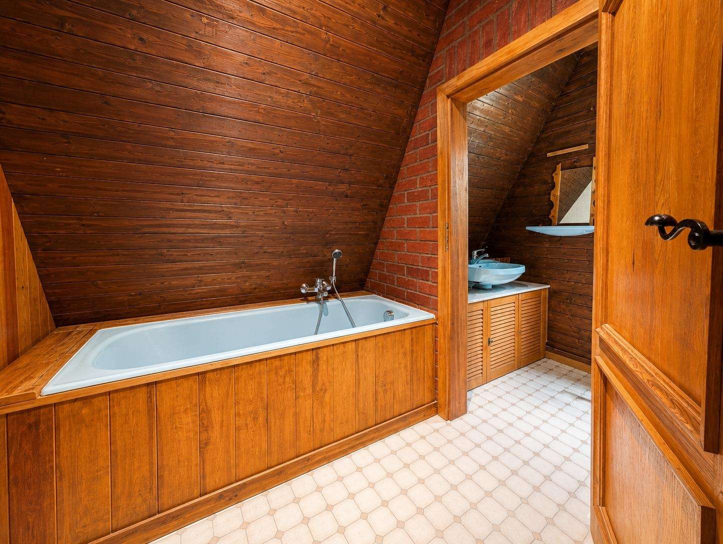 Wood-clad bathroom with a built-in white tub along a brick wall and a wooden vanity with a blue sink.