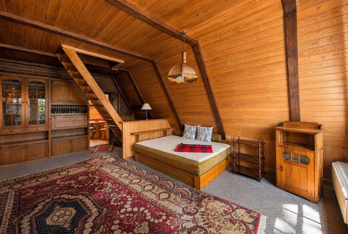 Cozy attic bedroom with wood-paneled walls, sloped ceiling, and a bed beside built-in cabinets and a warm rug.