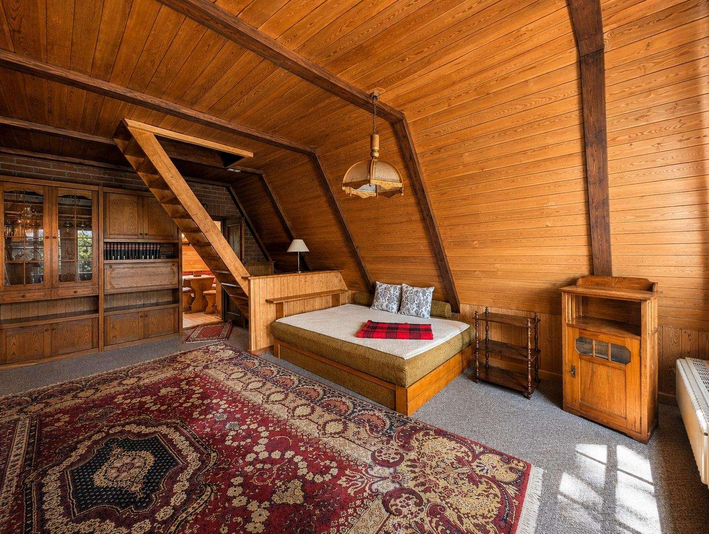 Cozy attic bedroom with wood-paneled walls, sloped ceiling, and a bed beside built-in cabinets and a warm rug.