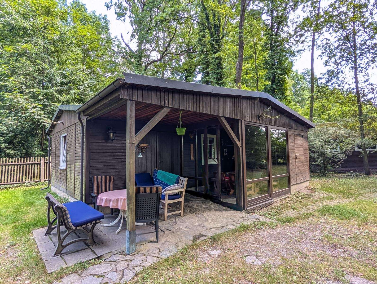 Wooden cabin with a covered porch in a green backyard; round table with pink tablecloth and several chairs outside.