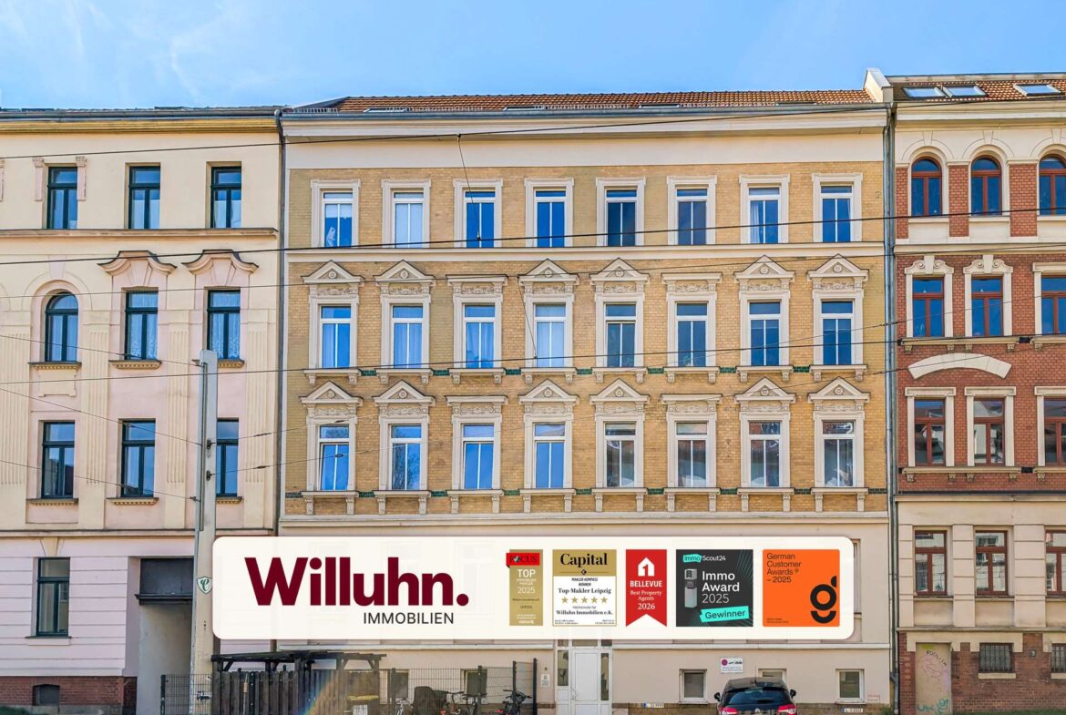 Row of historic European apartment buildings with decorative window frames and a large Willuhn Immobilien sign at street level.