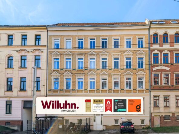 Row of historic European apartment buildings with decorative window frames and a large Willuhn Immobilien sign at street level.