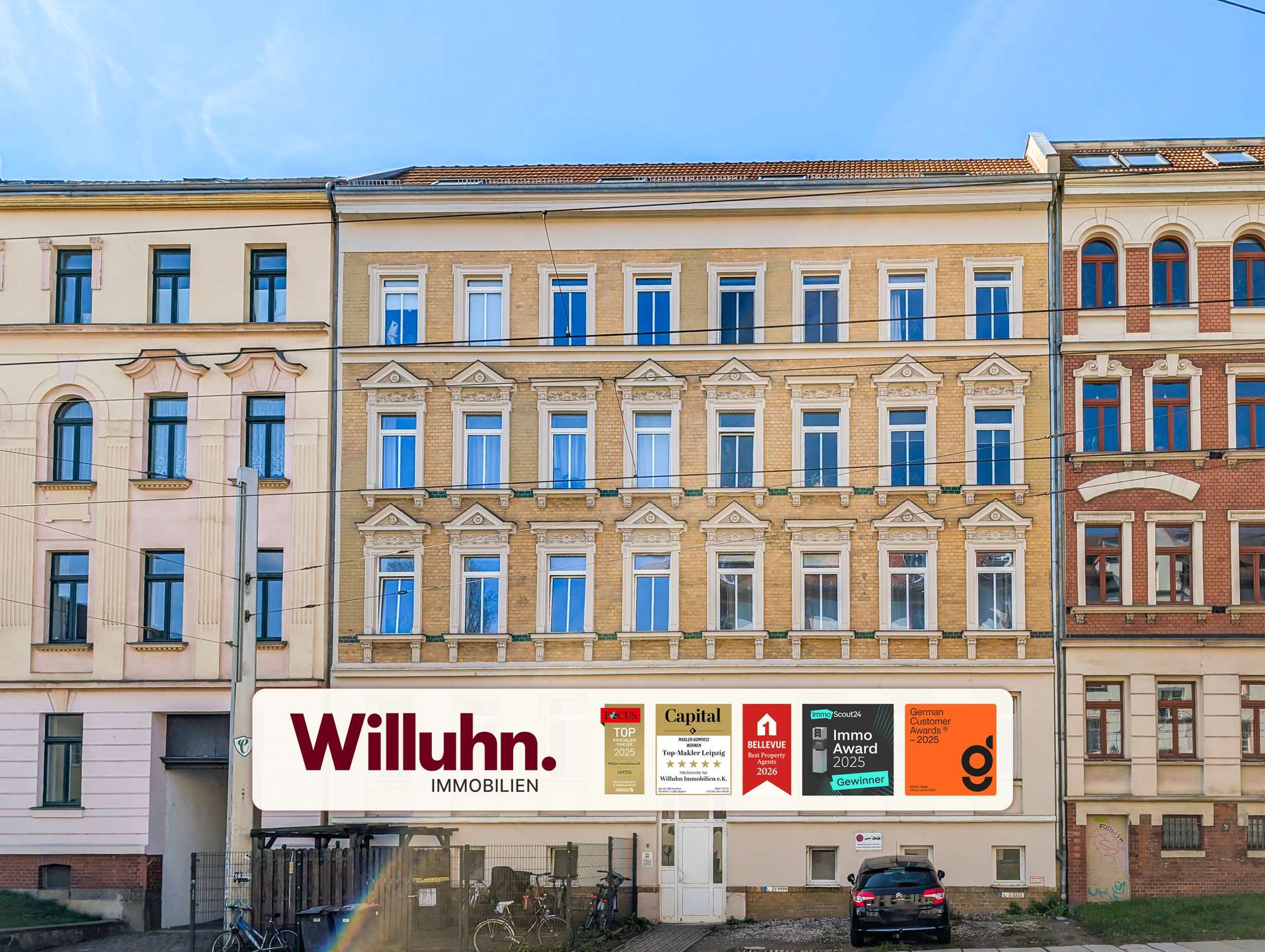 Row of historic European apartment buildings with decorative window frames and a large Willuhn Immobilien sign at street level.