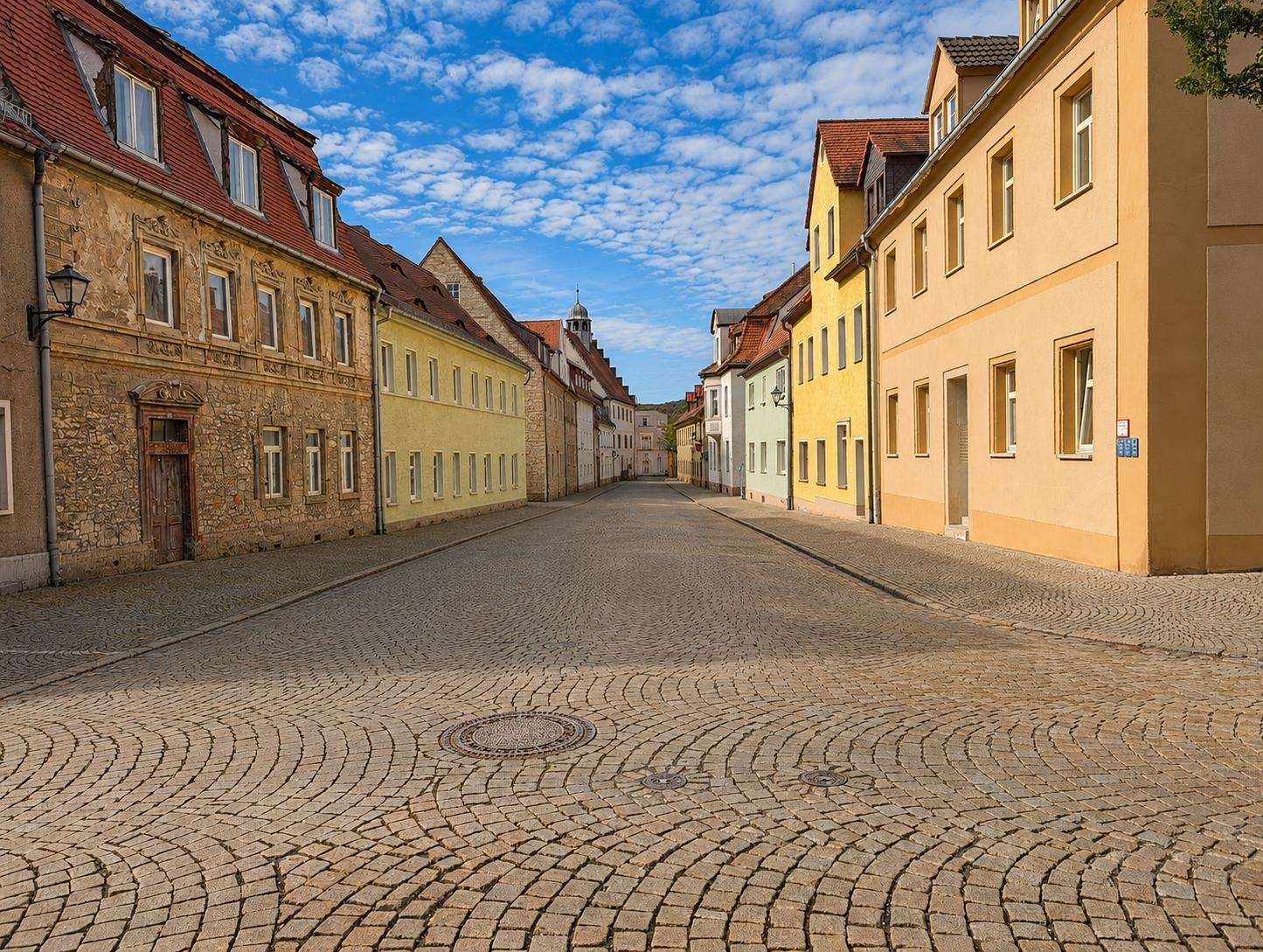 Sunlit cobblestone street lined with pastel houses in a quiet European town.