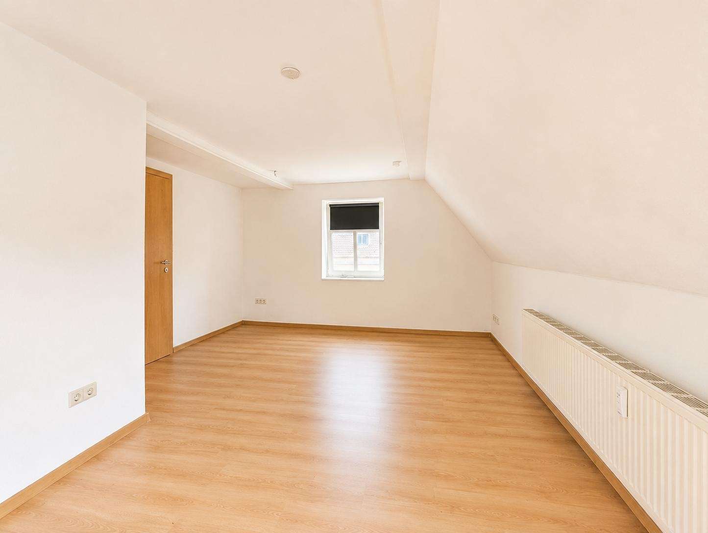 Unfurnished attic room with a sloped ceiling, light wood floor, a small window, and a radiator along the right wall.